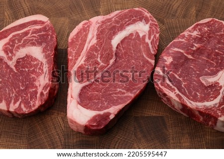 Close up three raw marbled ribeye beef steaks over end grain cutting board of wooden butcher block, high angle view, directly above Royalty-Free Stock Photo #2205595447