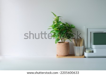 A potted plant, stationery and blank picture frame on white table Home office desk, copy space for your text.