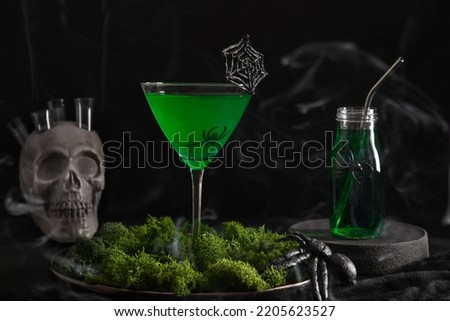 Halloween green cocktail with skull, spiders and smoke on black background.