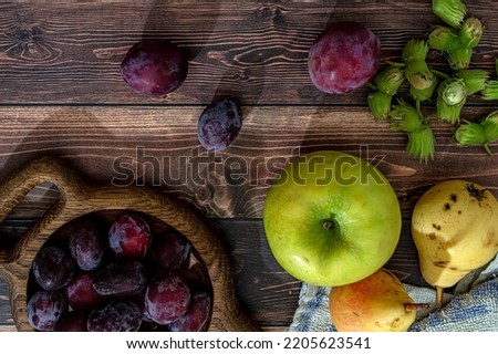 Fresh ripe plums, apples, pears and hazelnuts in a basket on a wooden table