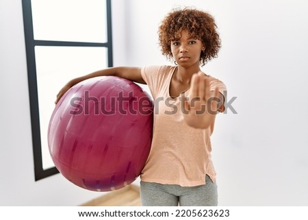Young african american woman holding pilates ball with open hand doing stop sign with serious and confident expression, defense gesture 