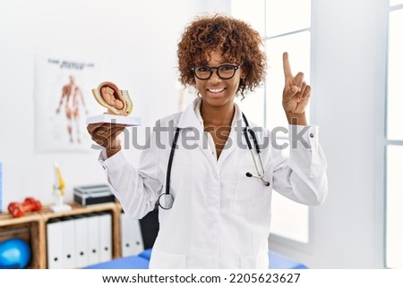 Young african american doctor woman holding anatomical model of female uterus with fetus smiling with an idea or question pointing finger with happy face, number one 
