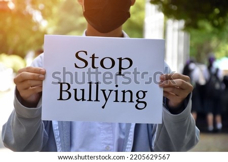 Asian boy student holds white paper which has texts 'Stop Bullying' inside, concept for protesting or calling out all people around the world to stop bullying people in different countries.