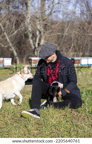 Stock photo of a smiling man sitting with his dogs and cuddling in a green field, feeling calm on a sunny autumn day.