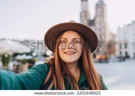 Young woman tourist in hat making selfie photo in front of the famous St. Mary's Basilica on the Market square in Krakow, Poland. Traveling Europe in autumn.