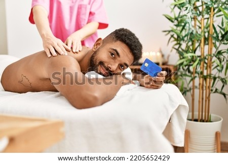 Young african american reciving back massage and holding credit card at beauty center.