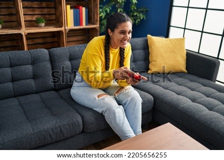 Young hispanic woman playing video game sitting on sofa at home