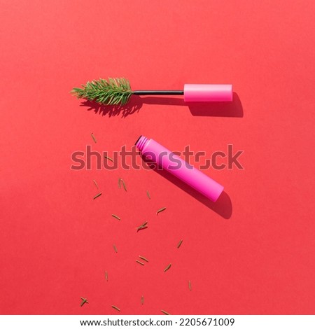Christmas tree branch with pink mascara and fir needles on pink background. Minimal winter holidays make up concept. Creative New Year celebration aesthetic. Flat lay.