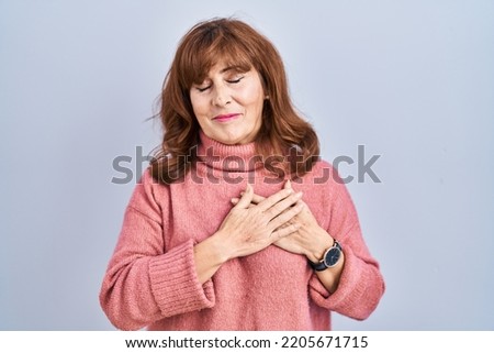 Middle age hispanic woman standing over isolated background smiling with hands on chest with closed eyes and grateful gesture on face. health concept. 
