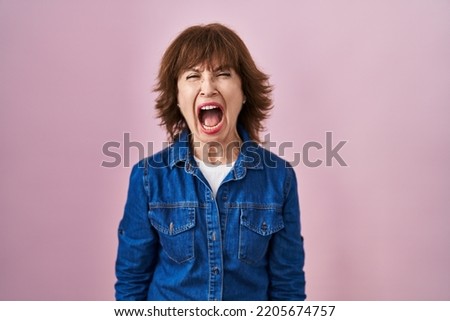 Middle age woman standing over pink background angry and mad screaming frustrated and furious, shouting with anger. rage and aggressive concept.  Royalty-Free Stock Photo #2205674757