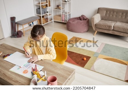 Minimal high angle portrait of teenage girl drawing pictures at table in cozy room, copy space