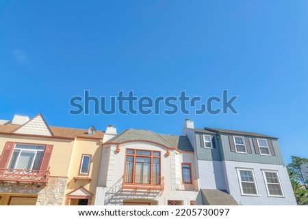 Three houses in a low angle view with different wall sidings in San Francisco, California. There are two houses on the side with fake window shutters and house in the middle with window railings.