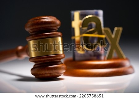 Judge's gavel with dollars in roll with single word tax  against gray background Royalty-Free Stock Photo #2205758651