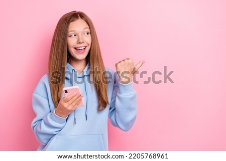 Photo of young pretty girlish little schoolgirl lady look interested finger point empty space ad hold phone user addicted shopaholic isolated on pink color background