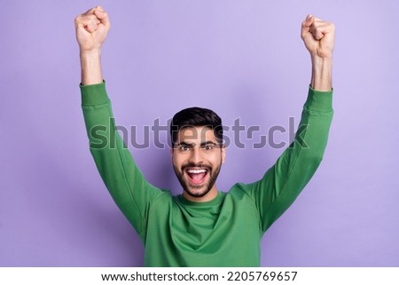 Photo of astonished handsome positive stylish guy dressed green pullover raising fists up screaming isolated on violet color background