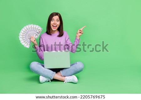 Full size photo of young pretty adorable gorgeous nice woman sitting using laptop crazy finger directing empty space much money bet isolated on green color background