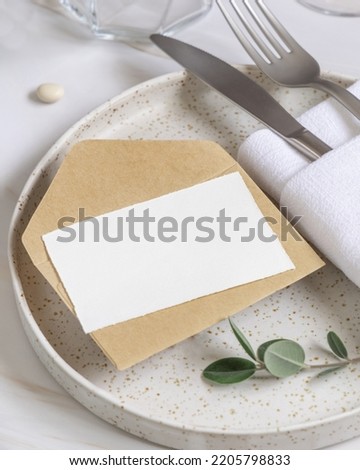 Elegant Table setting with card and envelope decorated with eucalyptus branches close up, Wedding Mockup. Romantic table with horizontal paper card. Close to nature and simplicity concepts