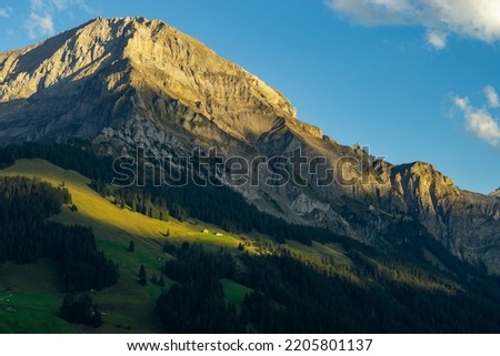 the morning sun illuminate the clouds and the peaks of Swiss mountains around Adelboden. first light in the valley from Boden, under the high mountain big wager, with green meadows, forests and rocks Royalty-Free Stock Photo #2205801137