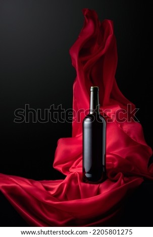 Bottle of red wine on a black background with flutters red cloth. Copy space.