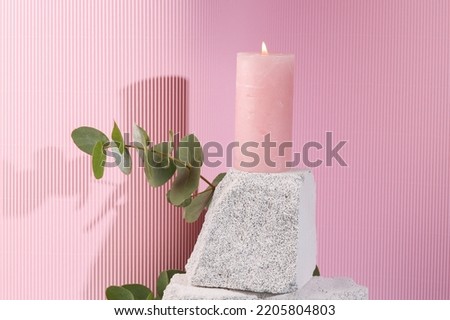 Flaming aroma candle on a stone podium with a sprig of eucalyptus. Aesthetic layout. Minimalistic beauty scene.