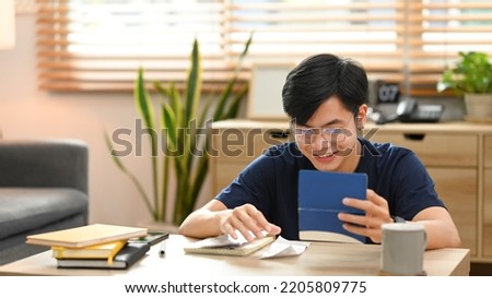 Happy asian man calculating money bank loan and managing expenses finances in living room. Household finance concept Royalty-Free Stock Photo #2205809775