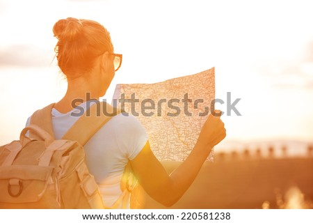 Back side of traveler girl searching right direction on map, bright orange sunset light, traveling along Europe, freedom and active lifestyle concept Royalty-Free Stock Photo #220581238