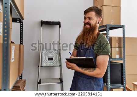 Young redhead man business worker writing on clipboard at office