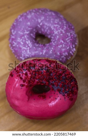Donuts With Pink and violet Icing And Colored Sprinkles with poppy seeds and dry raspberry on wooden background. Tasty delicious fat high calories sweet food. Selective Focus. favorite childhood treat