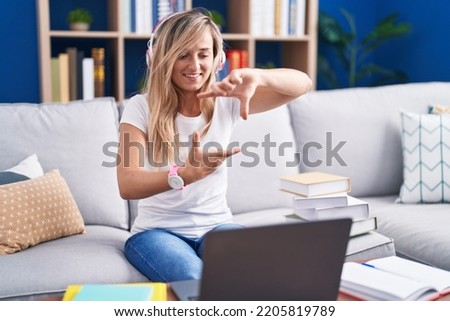 Young blonde woman studying using computer laptop at home smiling making frame with hands and fingers with happy face. creativity and photography concept. 