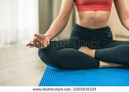 Close up shot of asian girl's hand doing yoga at home. She is stretching on a blue yoga mat. She is wearing fitness clothing.
