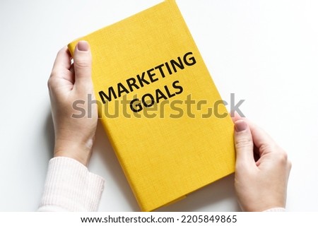 Mans hand drawing Marketing goals concept on white notebook