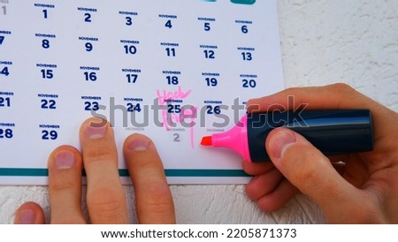 Close-up of the wall calendar November page 2022 and two male hands mark Black Friday date with a marker pen on it