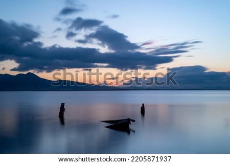Long exposure photography, sunken boat on blue sea with a city view on background moving clouds blurry concept