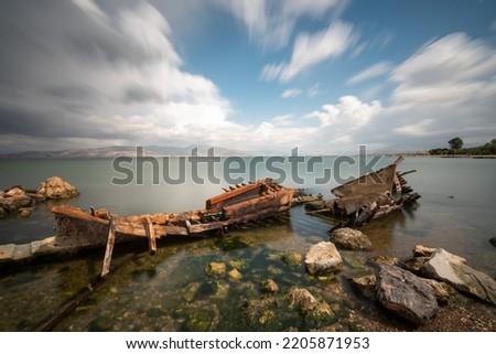 Long exposure photography, sunken boat on blue sea with a city view on background moving clouds blurry concept