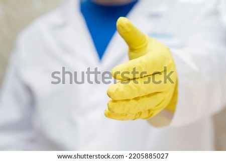 A doctor in a medical gown and protective gloves holds out his hand for a handshake. The face is not visible.