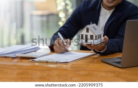 House model with agent business man signs a purchase contract or mortgage for a home, buy and sell home insurance concerning mortgage loan Real estate concept.