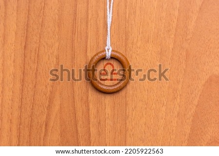 Shot of a pendant made with a wooden ring and a string, where a zodiac sign is engraved inside it, specifically the sign is Libra