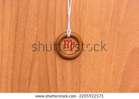 Shot of a pendant made with a wooden ring and a string, where a zodiac sign is engraved inside it, specifically the sign is Virgo