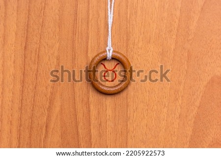 Shot of a pendant made with a wooden ring and a string, where a zodiac sign is engraved inside it, specifically the sign is Taurus