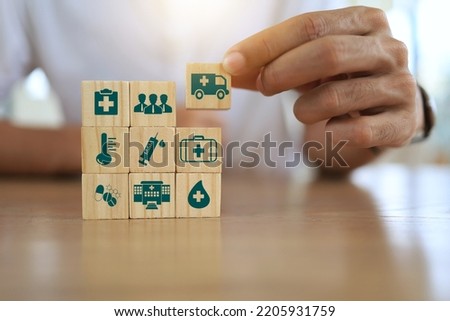 Man's hand on wooden blocks with icons of various types of insurance. Life health insurance and hospital concept.