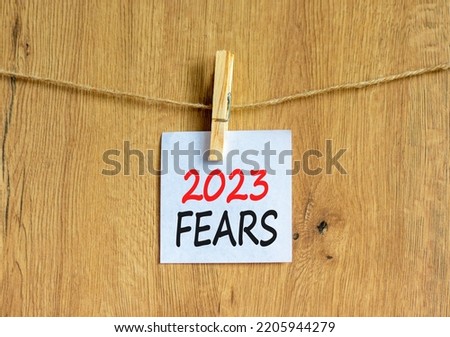 2023 Fears symbol. White paper with words 2023 Fears, clip on wooden clothespin. Beautiful wooden background. Business and 2023 fears concept. Copy space.