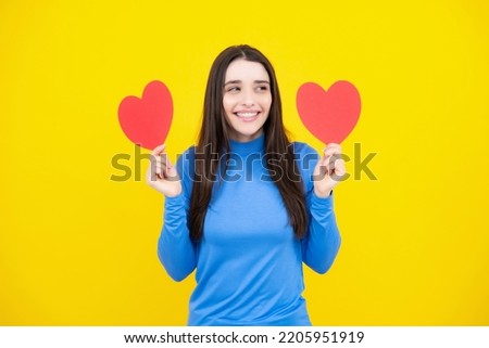 Love sign symbols for happy womens, valentines day or birthday. Beautiful young woman with heart in her hands. Attractive woman with paper heart over yellow background.