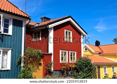 The facade of a red Swedish house with a blue house on the left and yellow houses on the right with orange brick roofs in Västervik, Sweden on a blue sky summer day Royalty-Free Stock Photo #2205953819