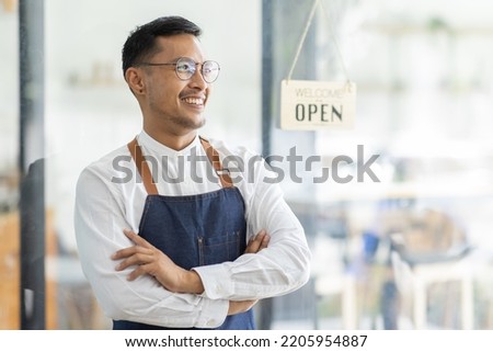 Asian Happy business man in glasses is a waitress in an apron, the owner of the cafe stands at the door with a sign Open waiting for customers , cafes and restaurants Small business concept.