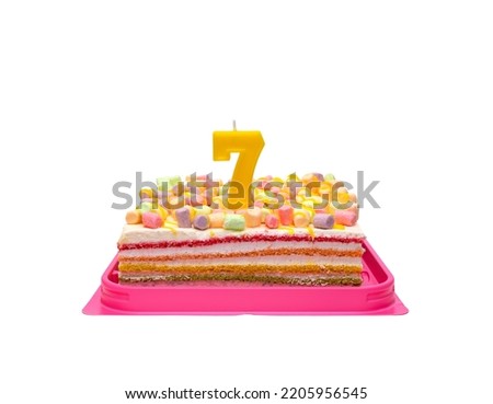 multi-colored rainbow cake in a transparent box with a red bow. Birthday cake with candle number 7 isolated on white background.