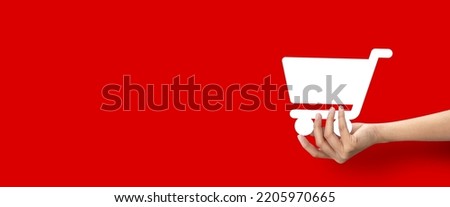 Hand holding shape of shopping cart icon on red background.