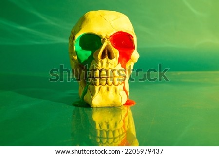 Skull with red and green paint leaking from eyes on green background.