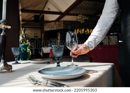 A young waiter in a stylish uniform is engaged in serving the table in a beautiful gourmet restaurant close-up. Table service in the restaurant. Royalty-Free Stock Photo #2205995303