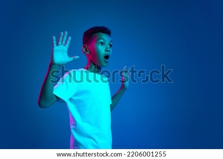 Shocked little boy, kid expressing emotions of surpise isolated over blue background in neon light. Education, childhood, modern lifestyle. Model is 7-8 years old looking away Royalty-Free Stock Photo #2206001255