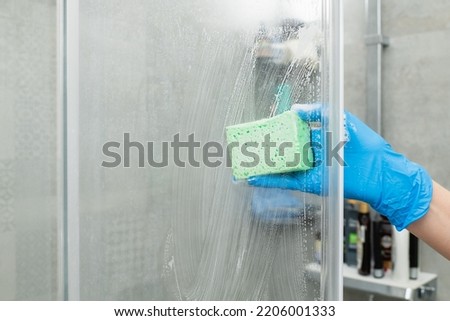 Woman in a blue glove cleans a shower cabin from limestone Royalty-Free Stock Photo #2206001333